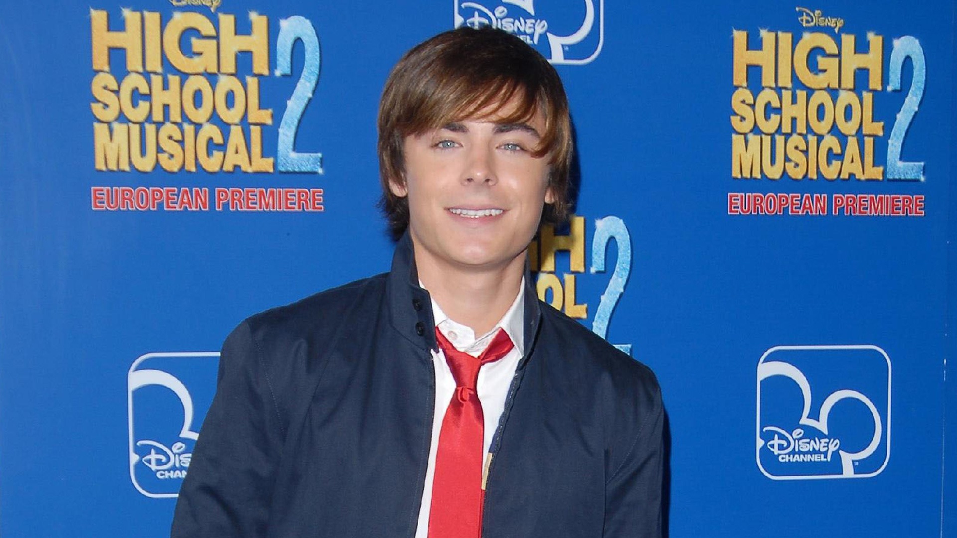 Zac Efron smiling and posing on the red carpet at the High School Musical 2 premiere.
