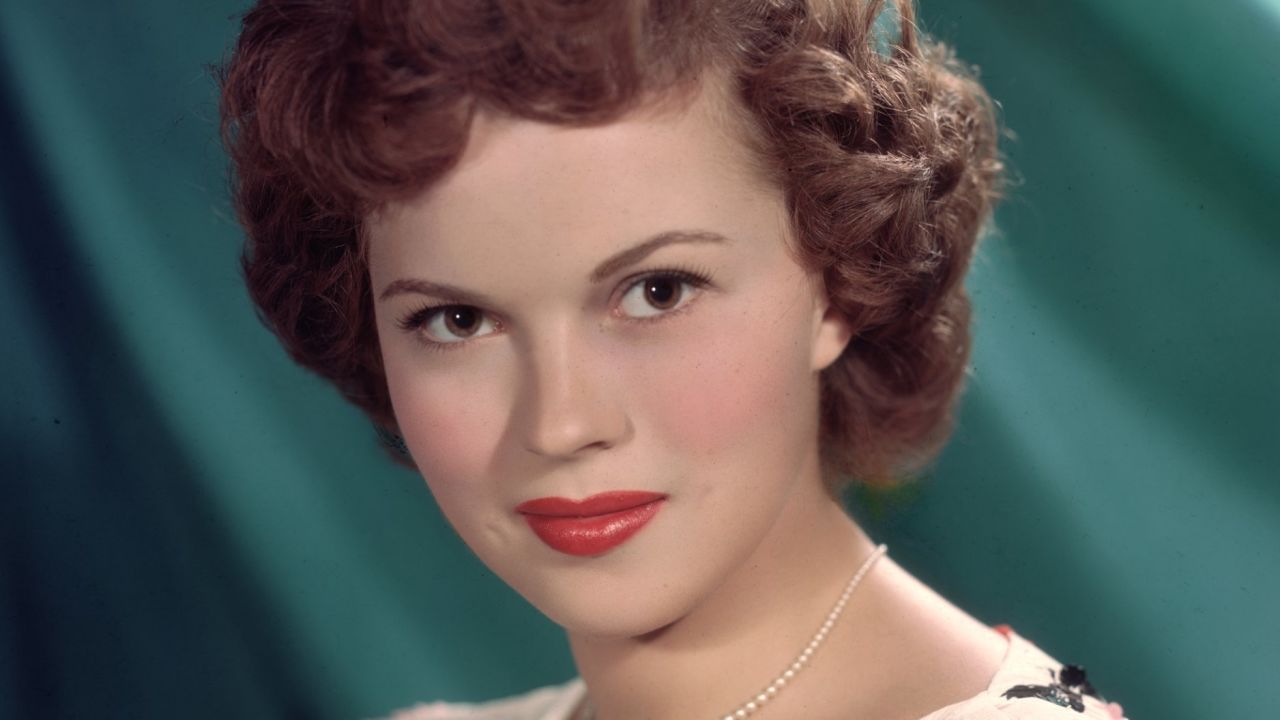 Teenage Shirley Temple glammed up, smiling brightly at the camera in a stylish outfit.