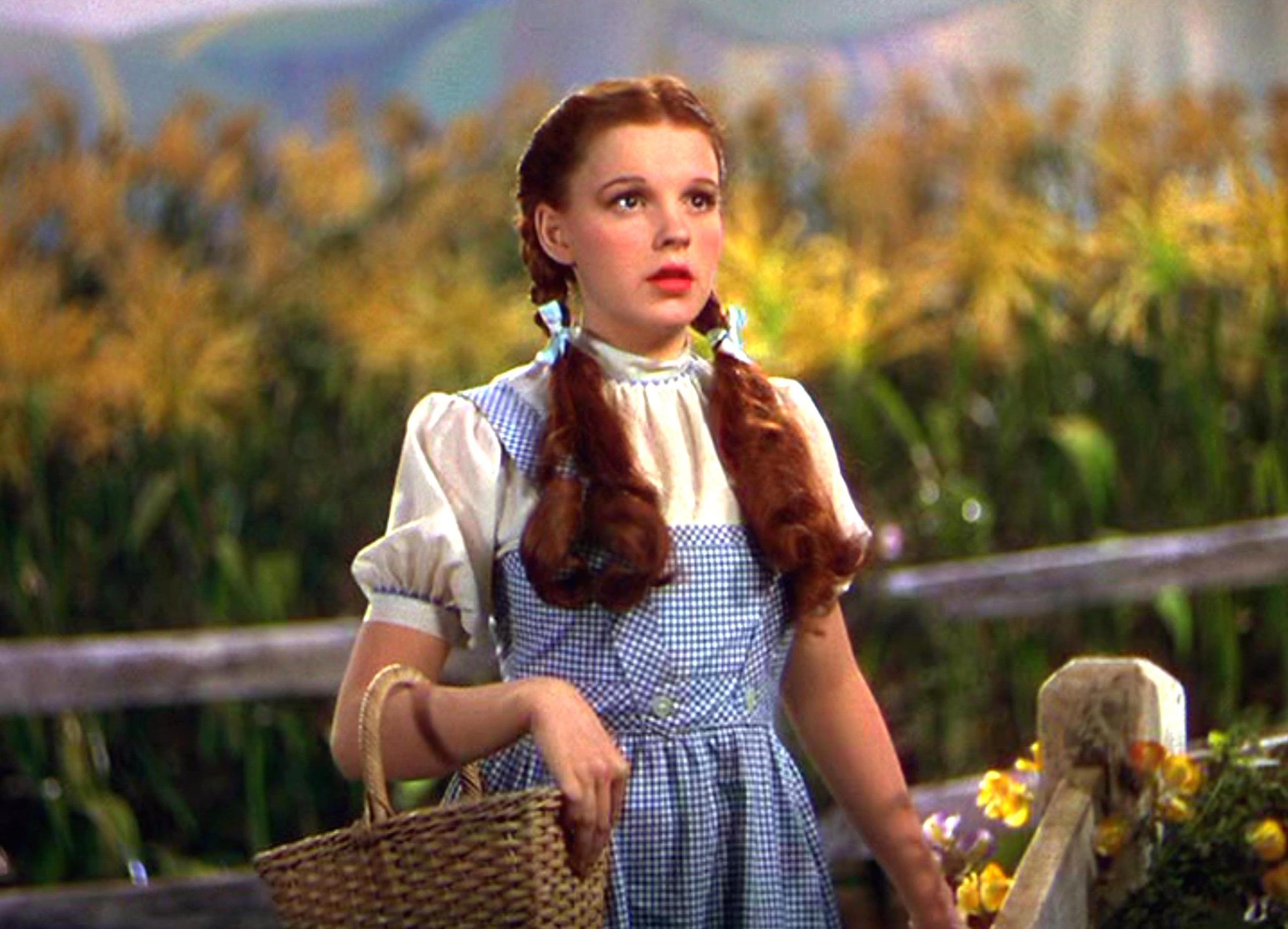 Judy Garland as Dorothy in The Wizard of Oz, holding her iconic basket and wearing the classic blue gingham dress.