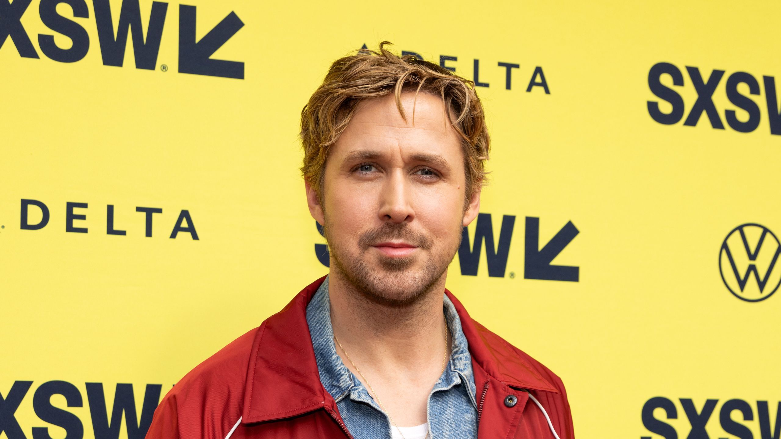Ryan Gosling dressed smart-casually on the red carpet against a bright yellow background.