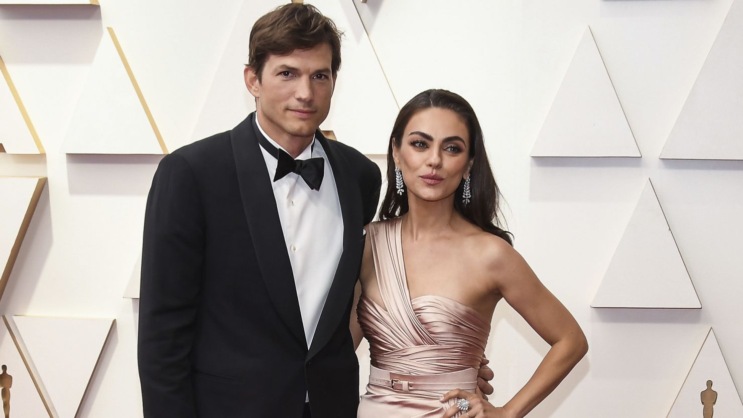 Mila Kunis and Ashton Kutcher posing together on the red carpet, looking stylish and radiant.