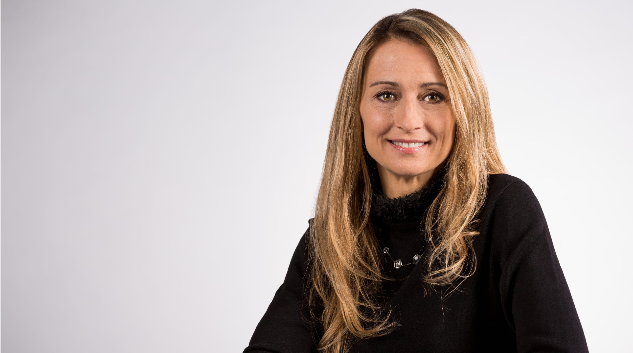 Colette Kress, Chief Financial Officer of NVIDIA, wearing a black sweater and smiling, seated in front of a light gray background.