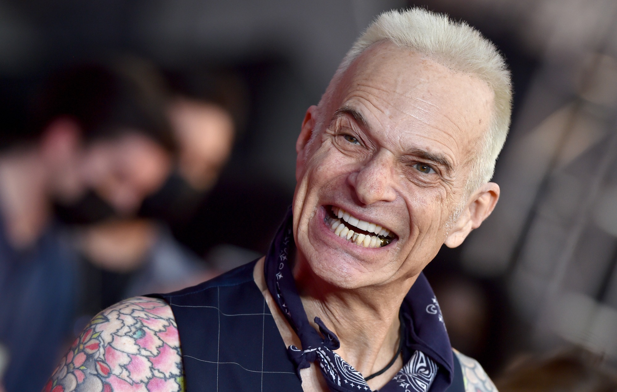 David Lee Roth smiling on the red carpet, wearing a vest and showing his tattooed arm, 2025.