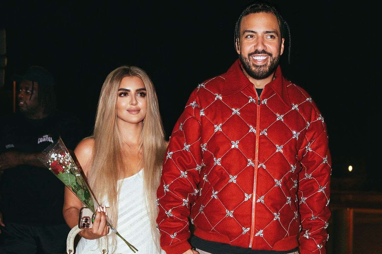 Rapper French Montana and Dubai Princess Sheikha Mahra walking together outdoors, smiling and holding hands, dressed stylishly.