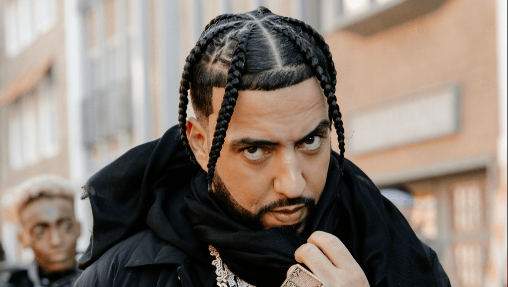 French Montana walking down the street, looking serious and focused at the camera.