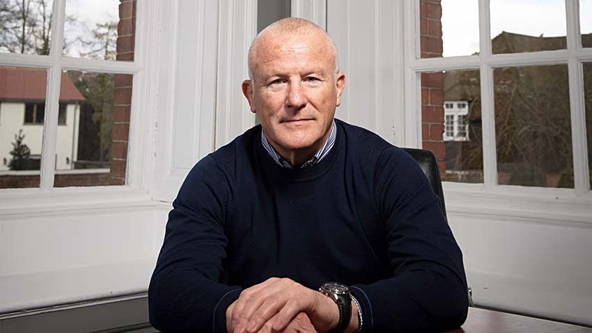 Neil Woodford sitting at his desk, posing confidently for the camera in a professional office setting.
