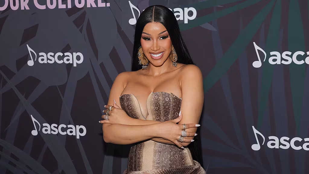 Cardi B posing on the red carpet, wearing a glamorous gown and smiling for photographers at a high-profile event.