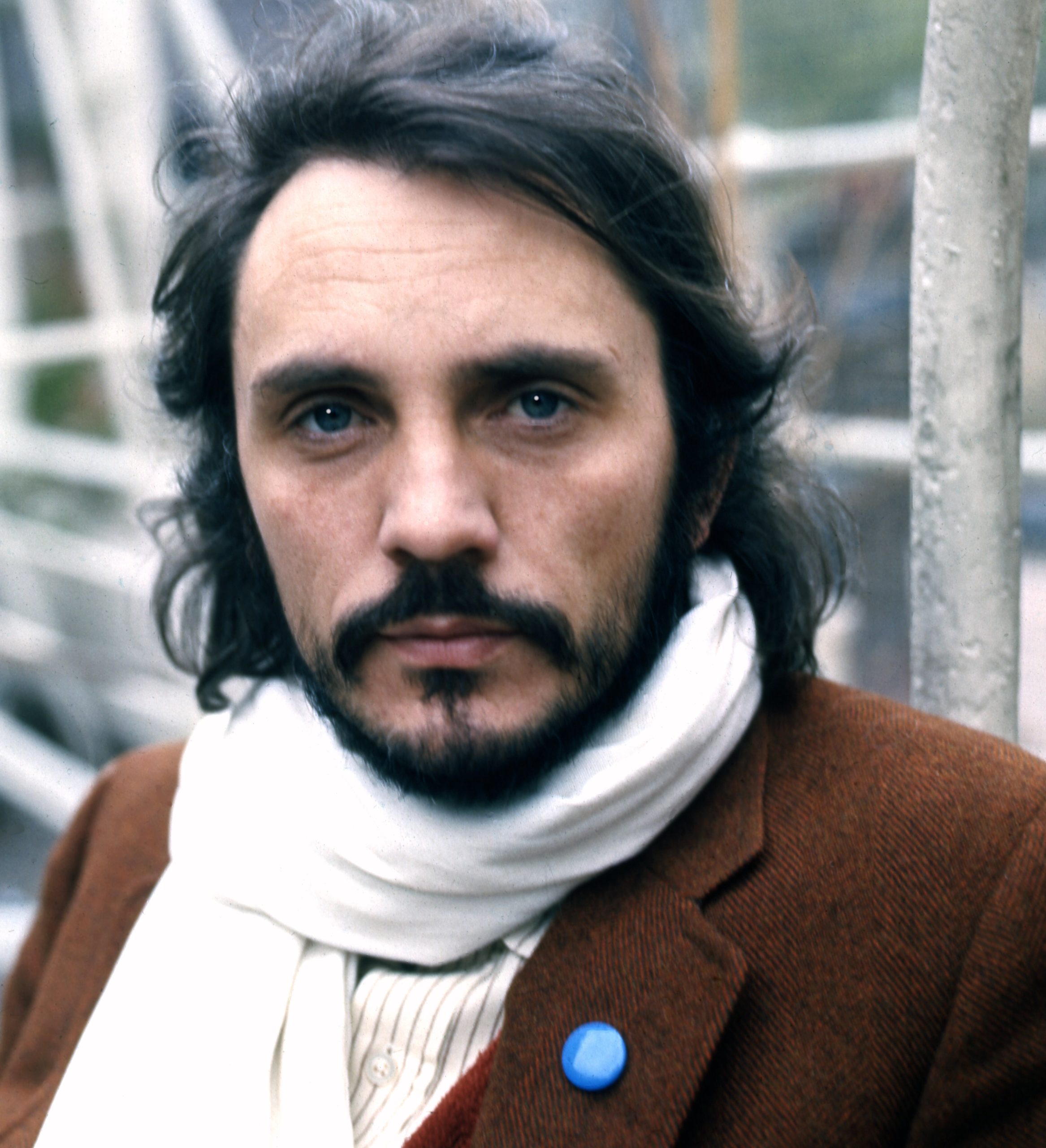 Terence Stamp with a beard and longer hair, wearing a brown jacket, posing for a portrait with a thoughtful expression.