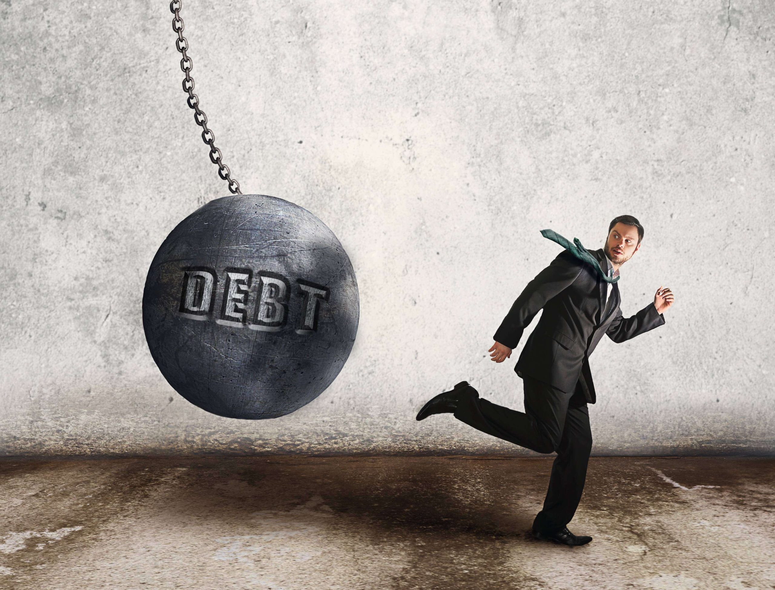 A man running away from a massive wrecking ball labeled “Debt,” symbolizing the pressure of financial obligations.