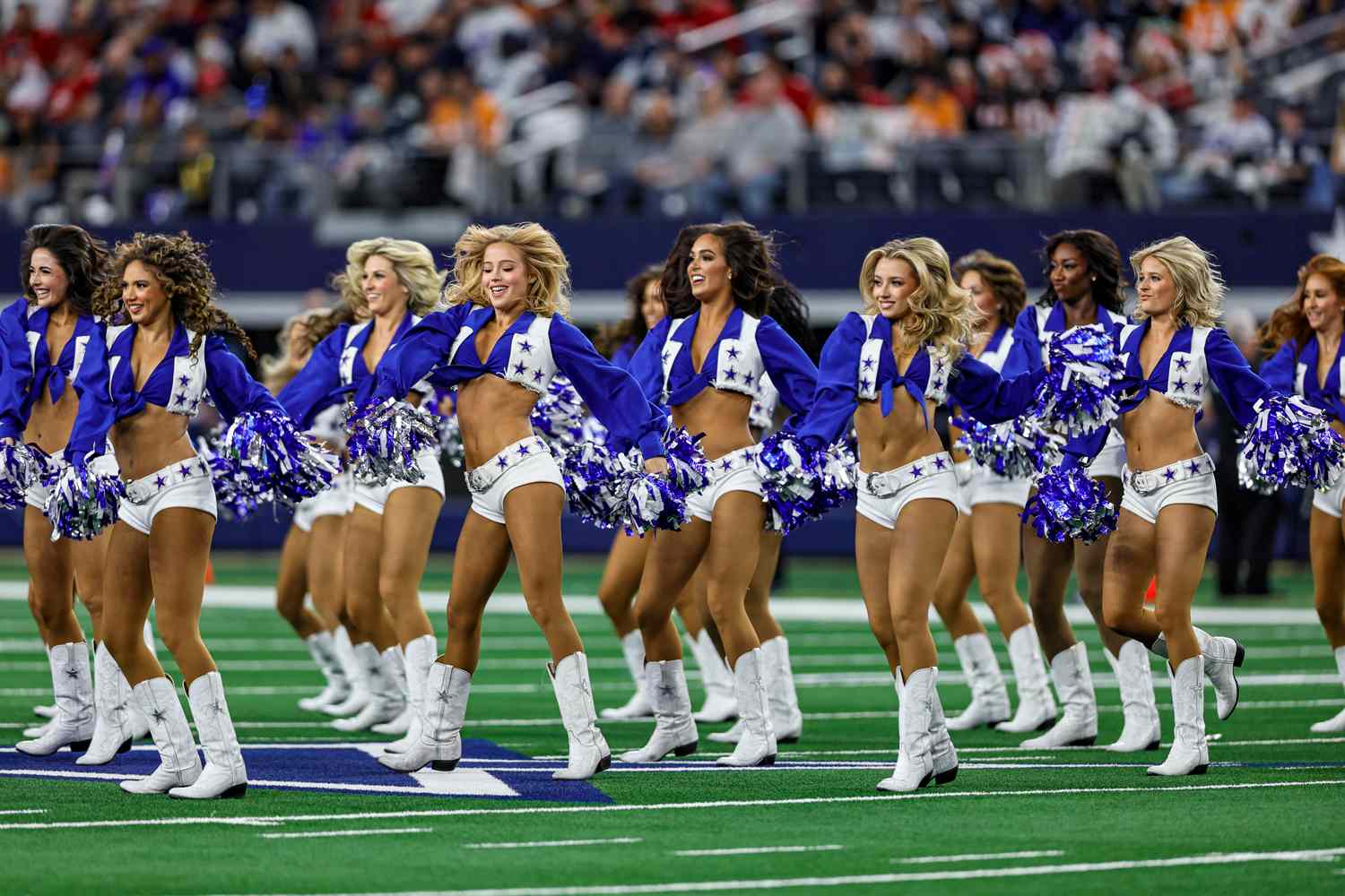 Dallas Cowboys Cheerleaders performing a synchronized routine on the field during an NFL game.