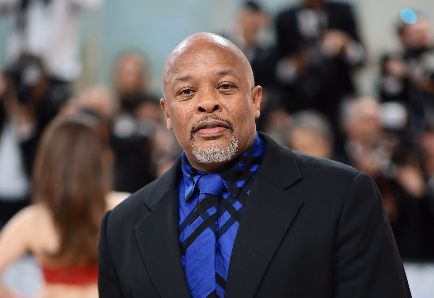 Dr. Dre attending a red carpet event in a black suit and blue patterned tie