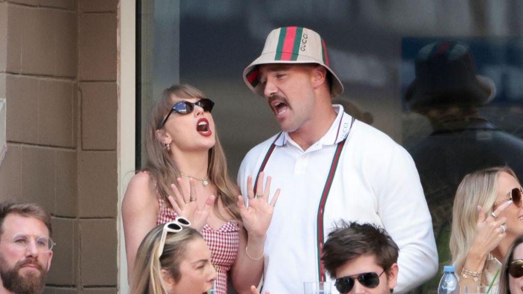 Taylor Swift and Travis Kelce singing together, smiling as the crowd cheers.