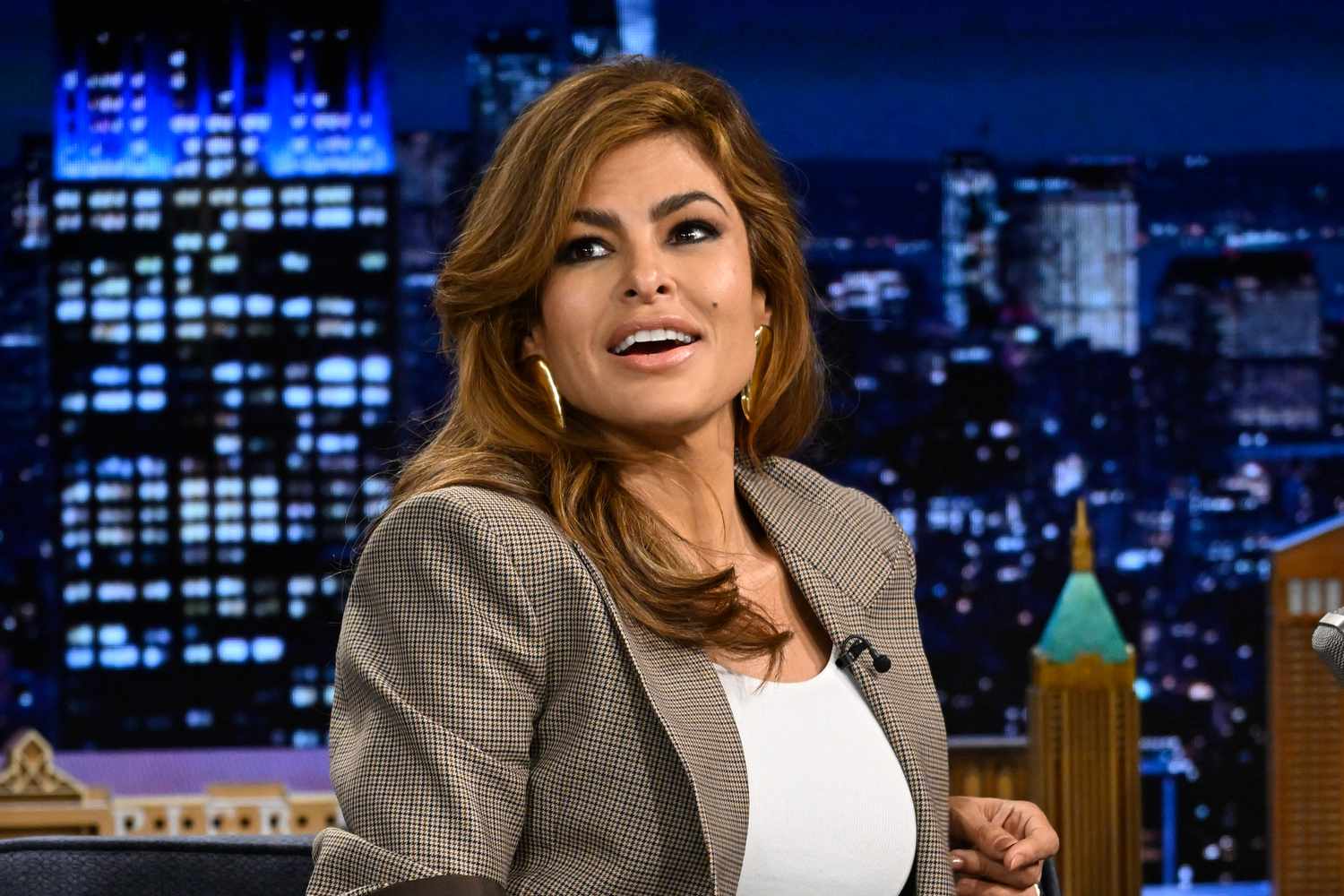 Eva Mendes smiling and gesturing while speaking to the audience during a late-night talk show appearance.