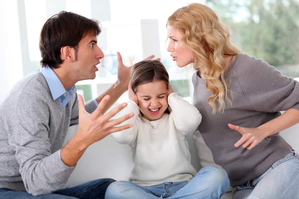 Parents arguing loudly while their young daughter covers her ears in distress.