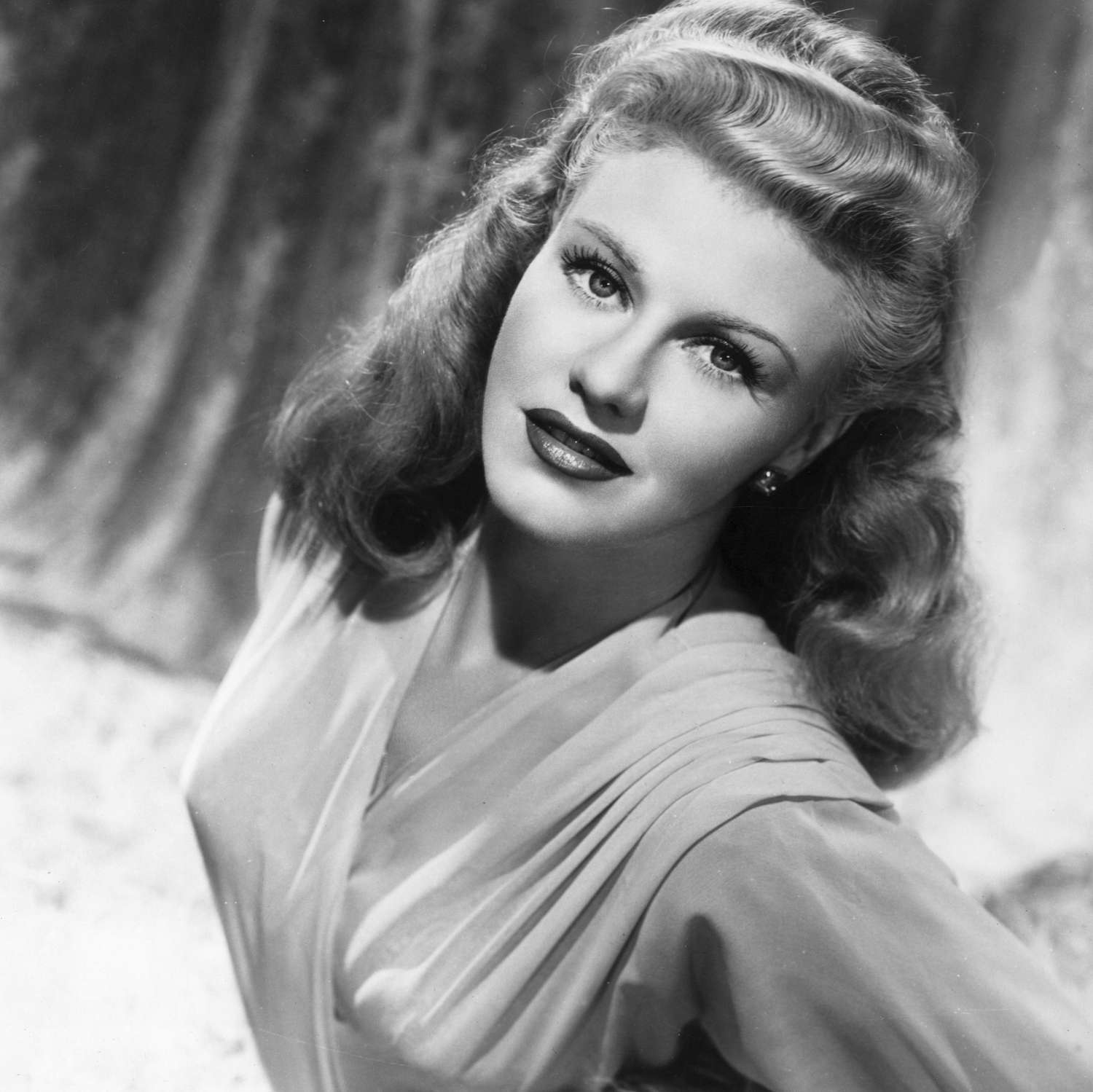 Black and white photo of Ginger Rogers smiling at the camera, looking glamorous and elegant in classic Hollywood style.