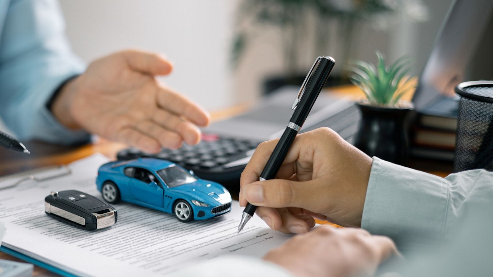 A hand holding a pen signing a contract for a new car purchase.
