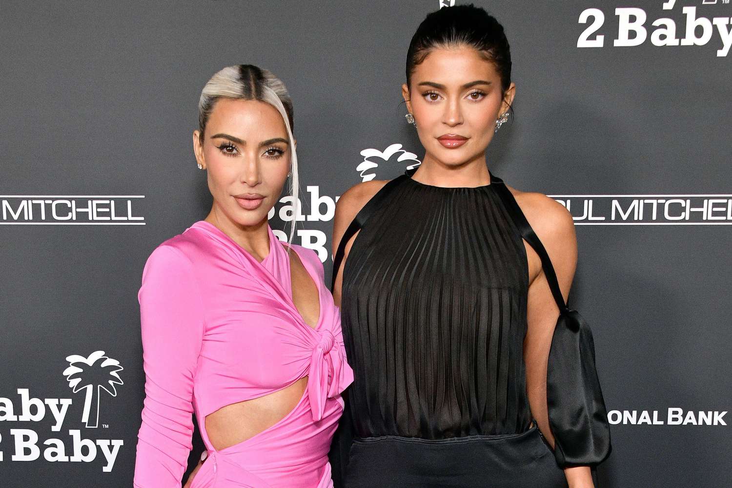 Kim Kardashian in pink and Kylie Jenner in black, both dressed elegantly on the red carpet, facing the paparazzi.