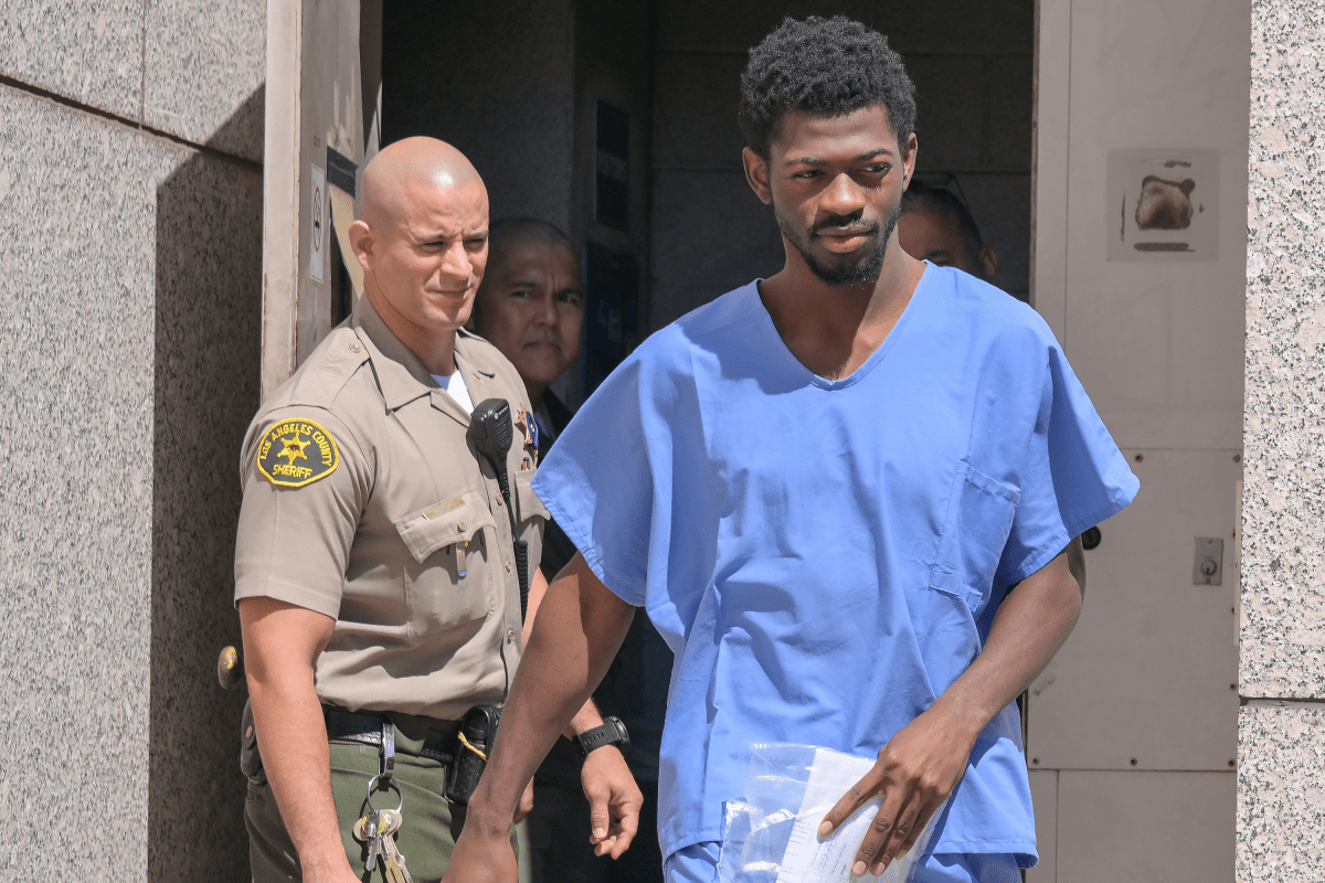 Lil Nas X leaving Van Nuys jail wearing prison scrubs and handcuffs, escorted by officers.