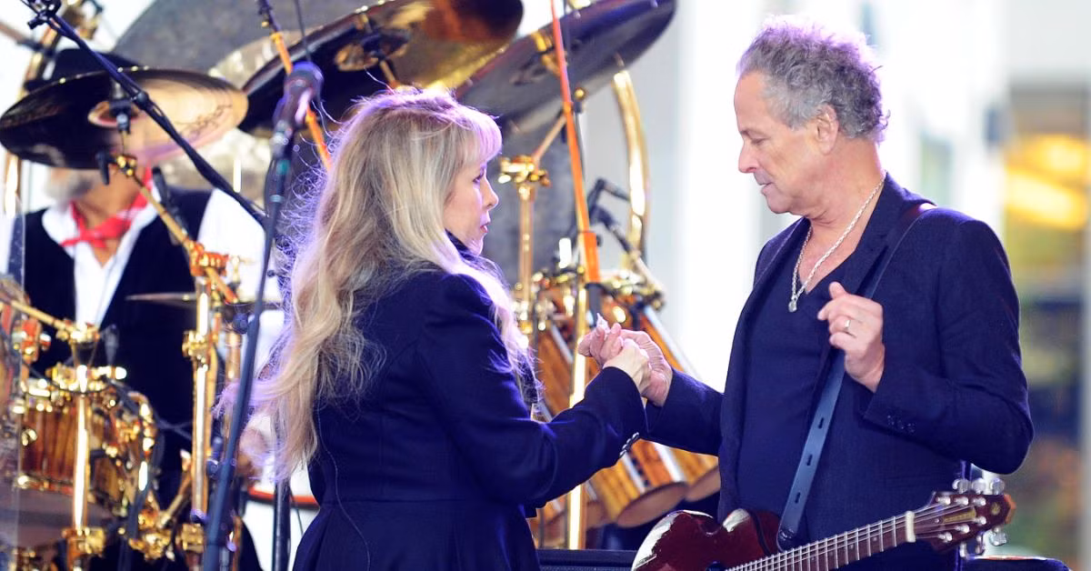 Stevie Nicks holding Lindsey Buckingham’s hand on stage during a Fleetwood Mac performance.