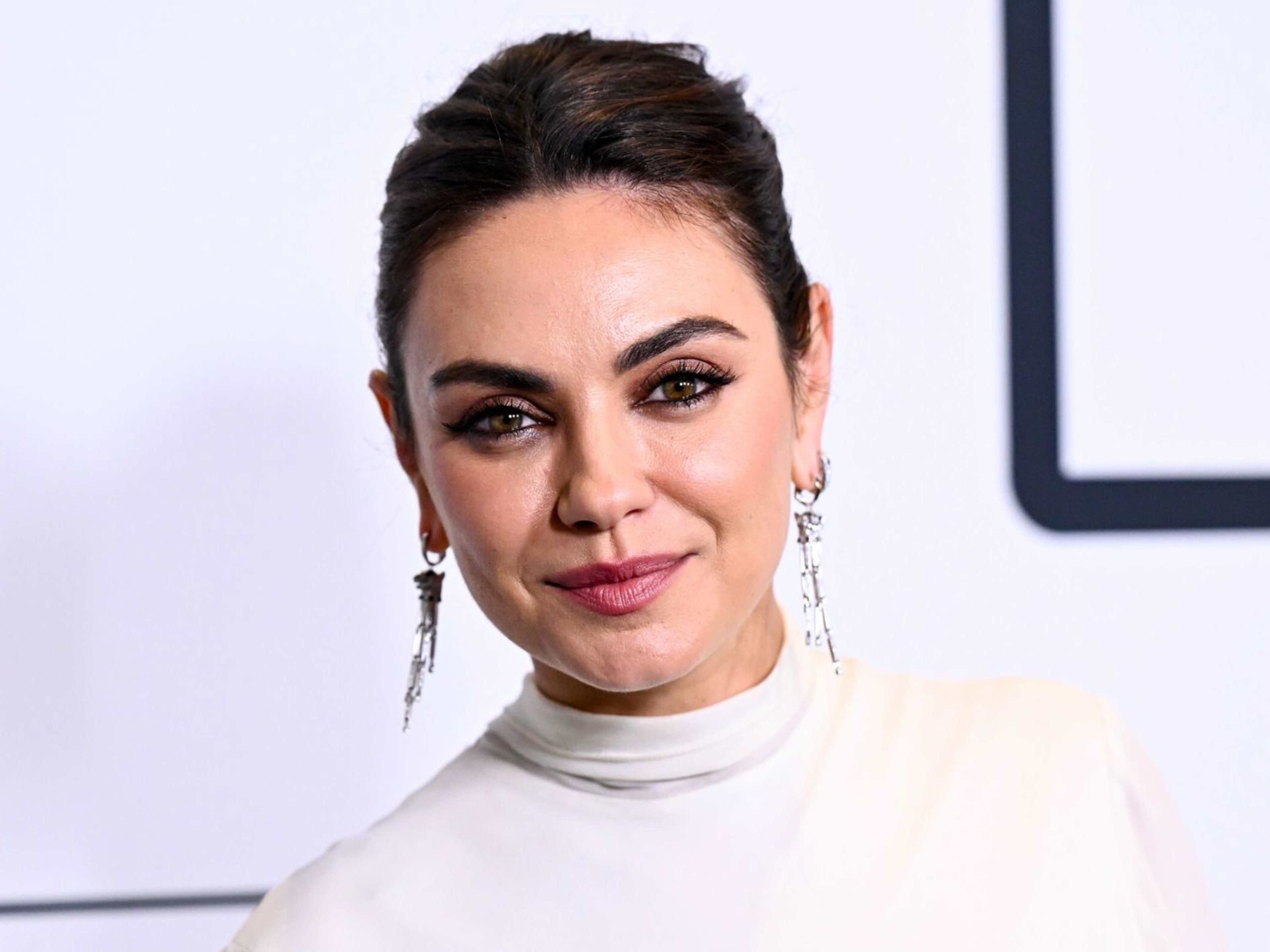 Mila Kunis all glammed up in an elegant gown, posing confidently on the red carpet at a glamorous event.