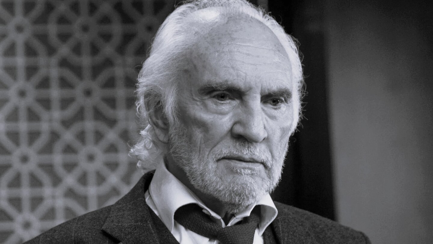 Terence Stamp in a black-and-white scene from Murder Mystery, dressed sharply and looking contemplative.