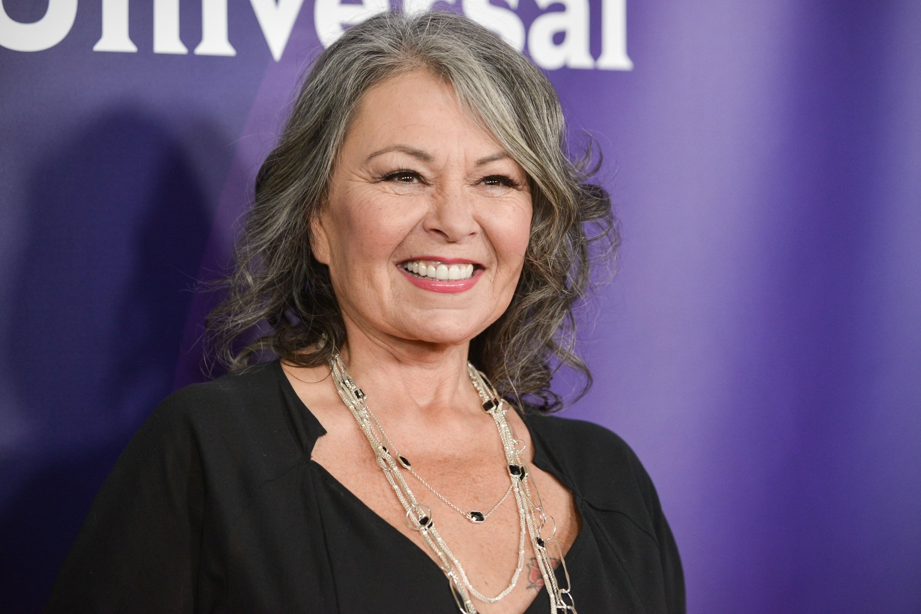 Roseanne Barr smiling and posing on the red carpet at a celebrity event, wearing a stylish outfit and glamorous makeup.