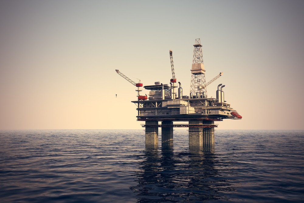 Massive offshore oil rig towering above the ocean, equipped with drilling platforms and machinery under a clear sky.