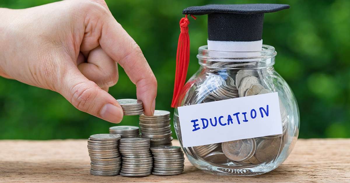 A hand stacking coins next to a savings jar labeled “Education” with a small graduation cap on top, symbolizing saving for college.