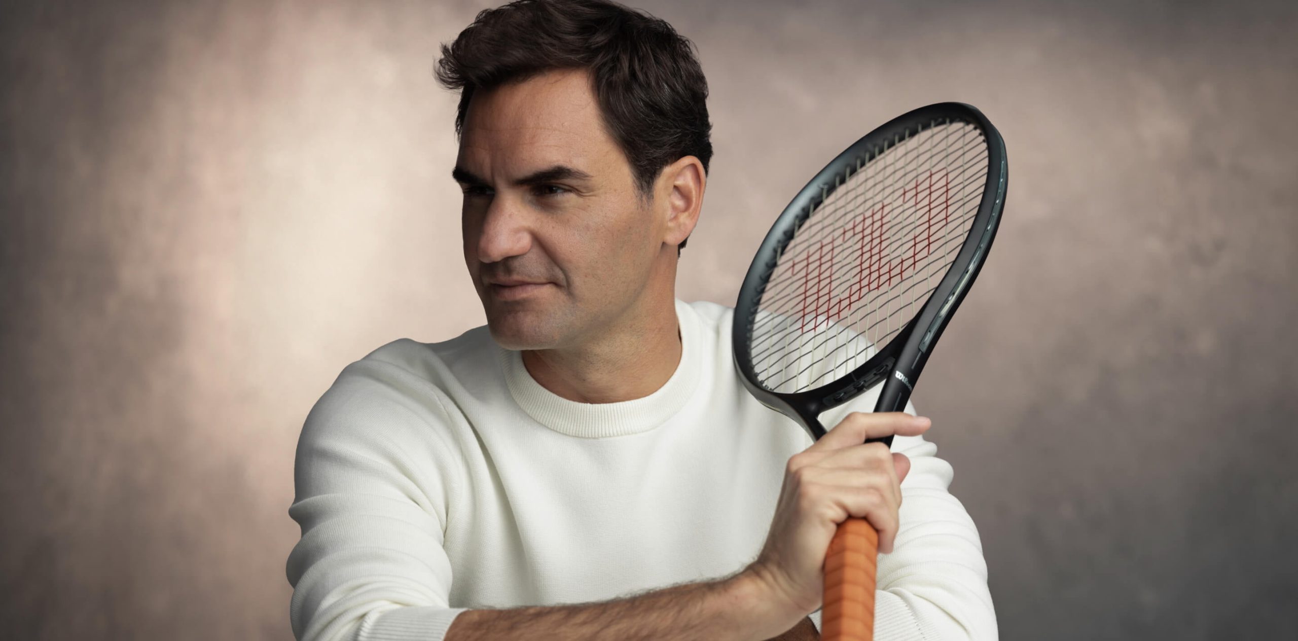 Roger Federer holding a tennis racket during a portrait session, wearing a white sweater.