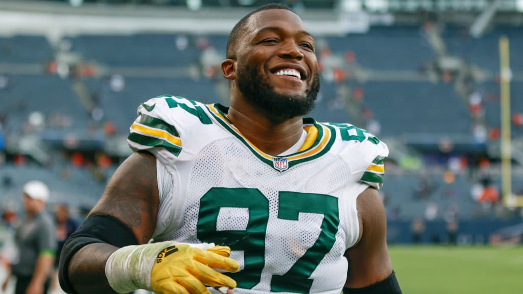 Kenny Clark running on the football field with a wide smile during a game.