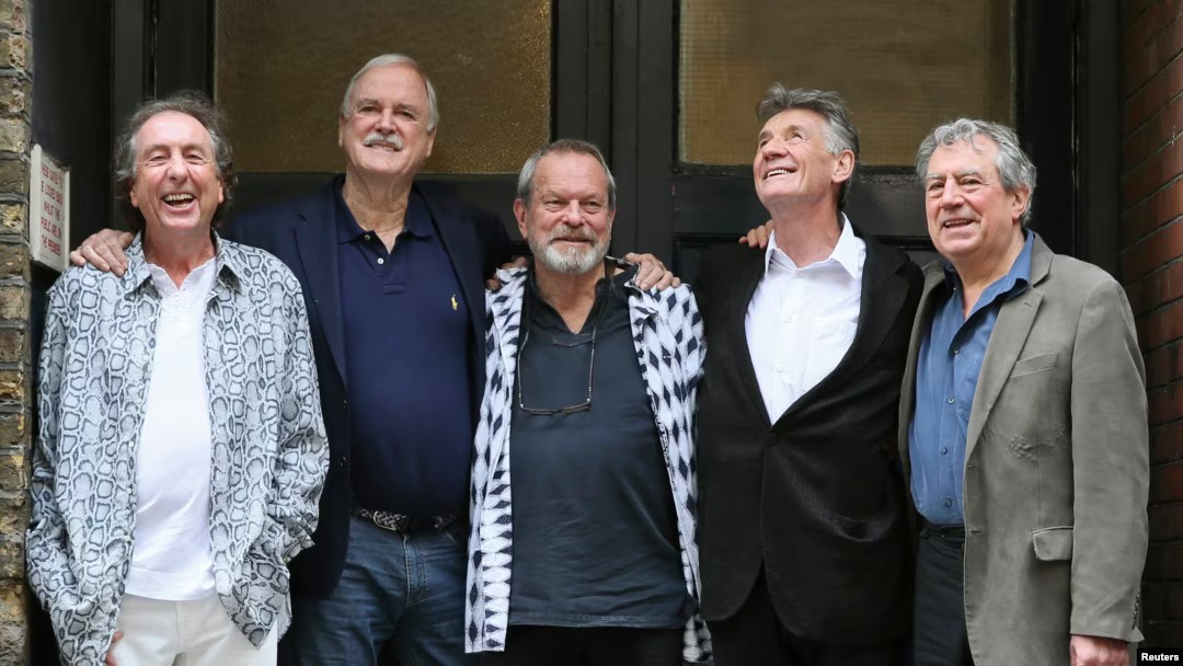 Monty Python group photo showing Eric Idle, John Cleese, Terry Gilliam, Michael Palin, and Terry Jones standing together and smiling during a reunion event.