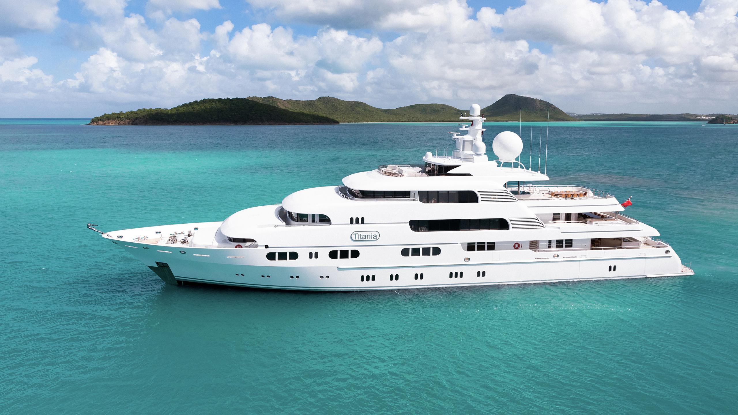 Aerial view of John Caudwell’s 240ft superyacht Titania sailing on clear blue waters.