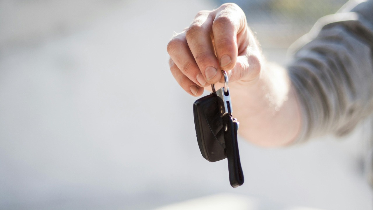 Person handing over car keys to a buyer in front of a new car, symbolizing a completed car purchase.