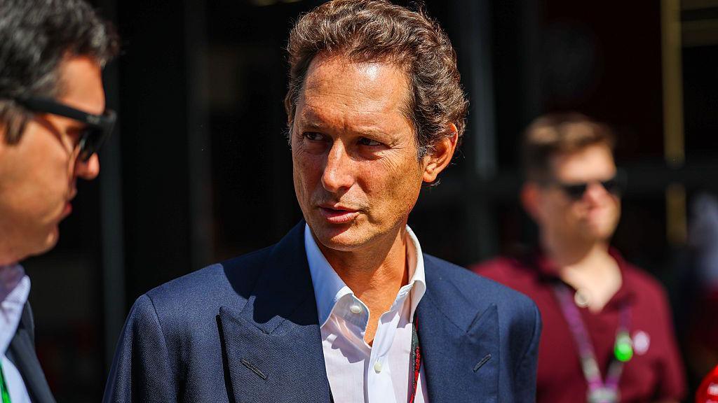 John Elkann in a dark suit walking out of a courthouse, looking composed as photographers capture the moment.