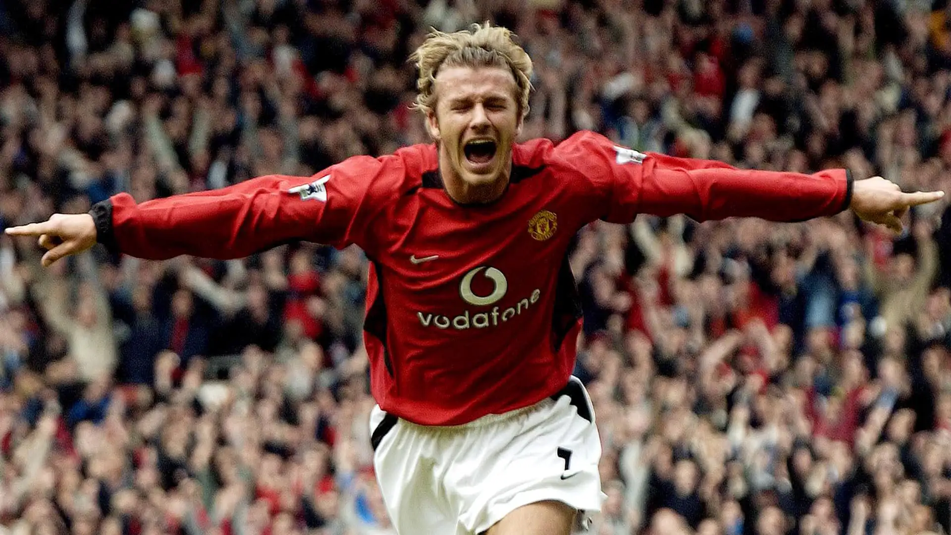 David Beckham celebrating a goal for Manchester United, jumping with arms raised in excitement on the pitch.