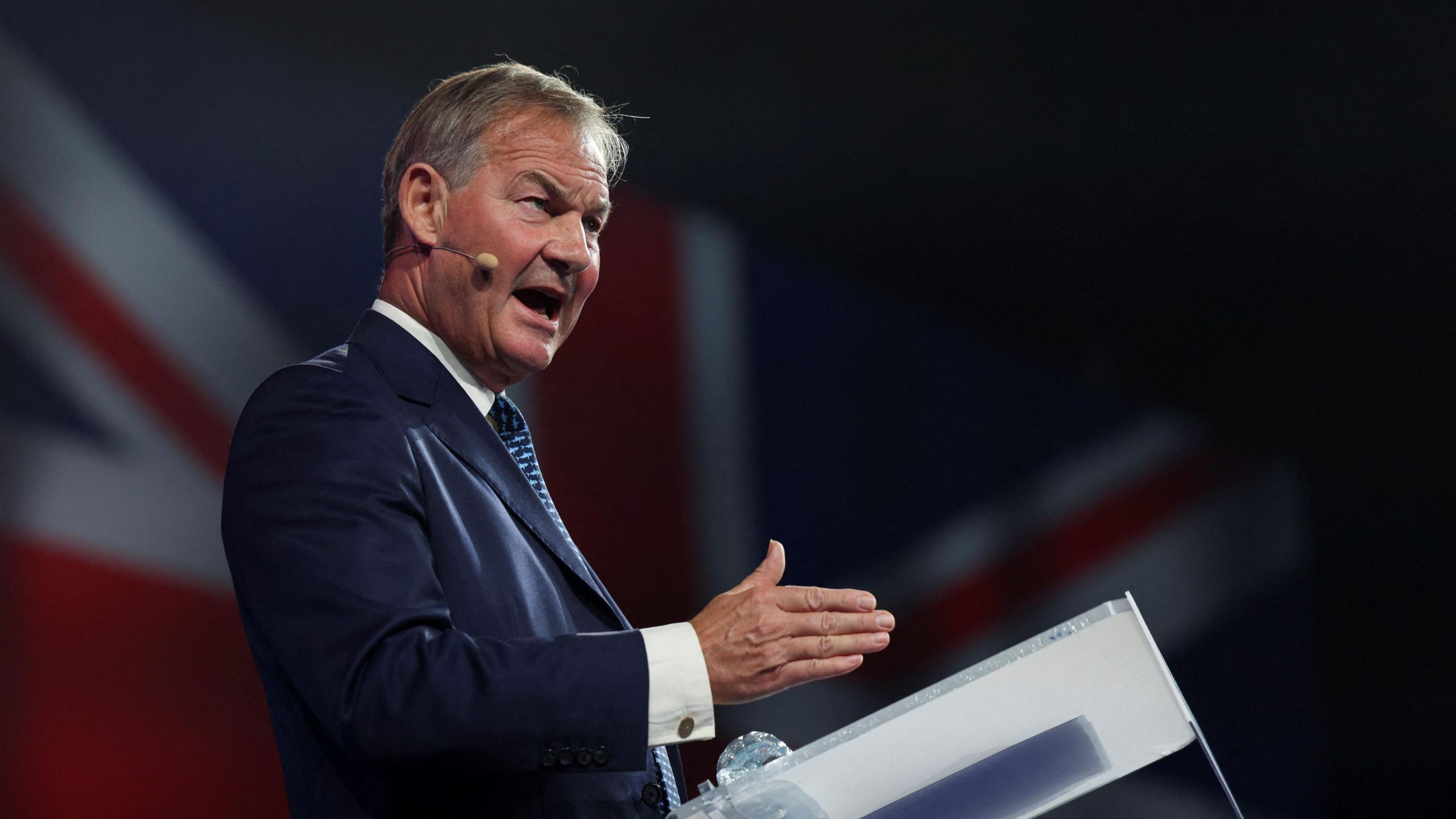 Rupert Lowe passionately delivering a speech, gesturing with his hands to emphasize key points.