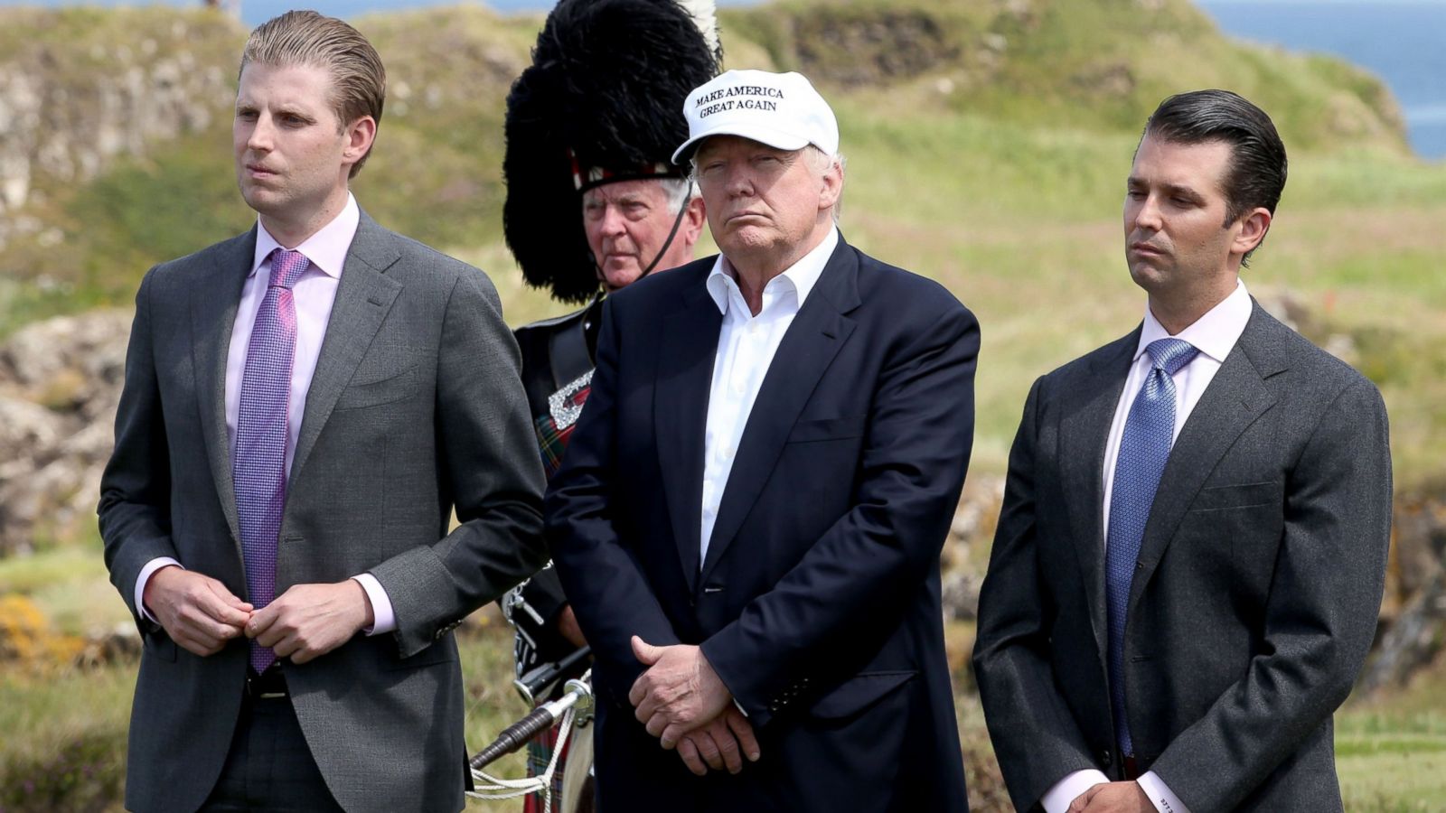 Donald Trump standing with Eric Trump and Donald Trump Jr. on either side of him, all three dressed in suits at a public event.