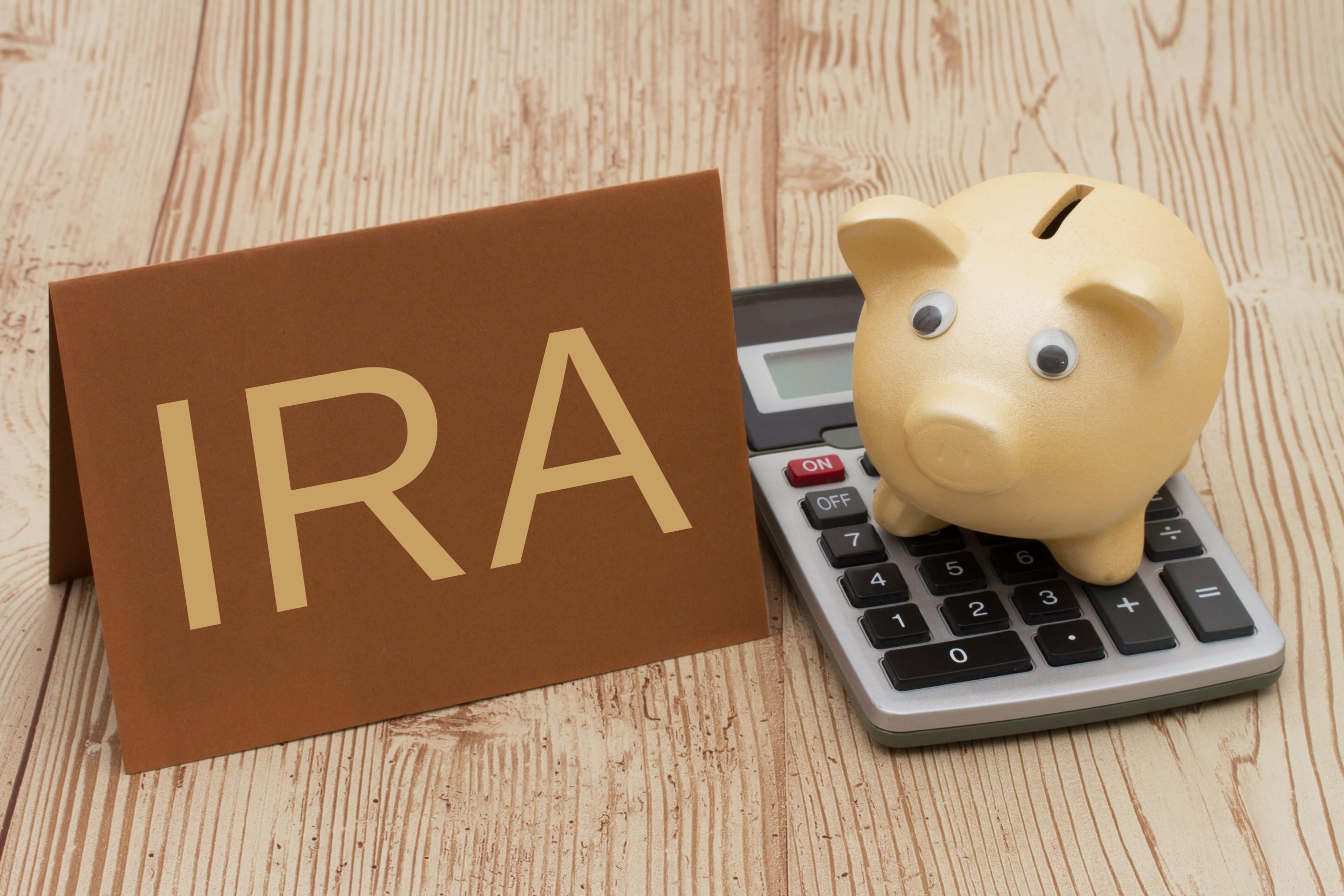 An IRA sign next to a piggy bank placed on a calculator, symbolizing retirement savings and financial planning.