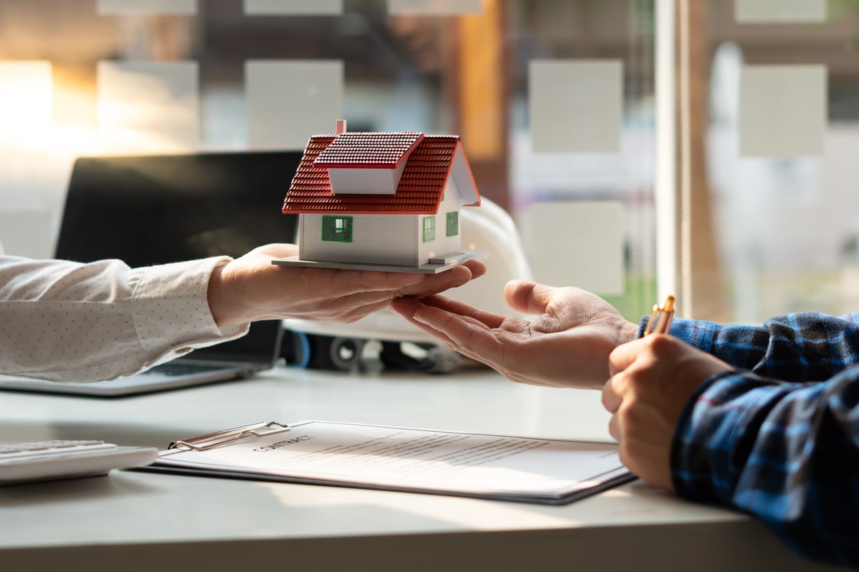 Bank manager handing a small house model to a customer, symbolizing the mortgage approval process.