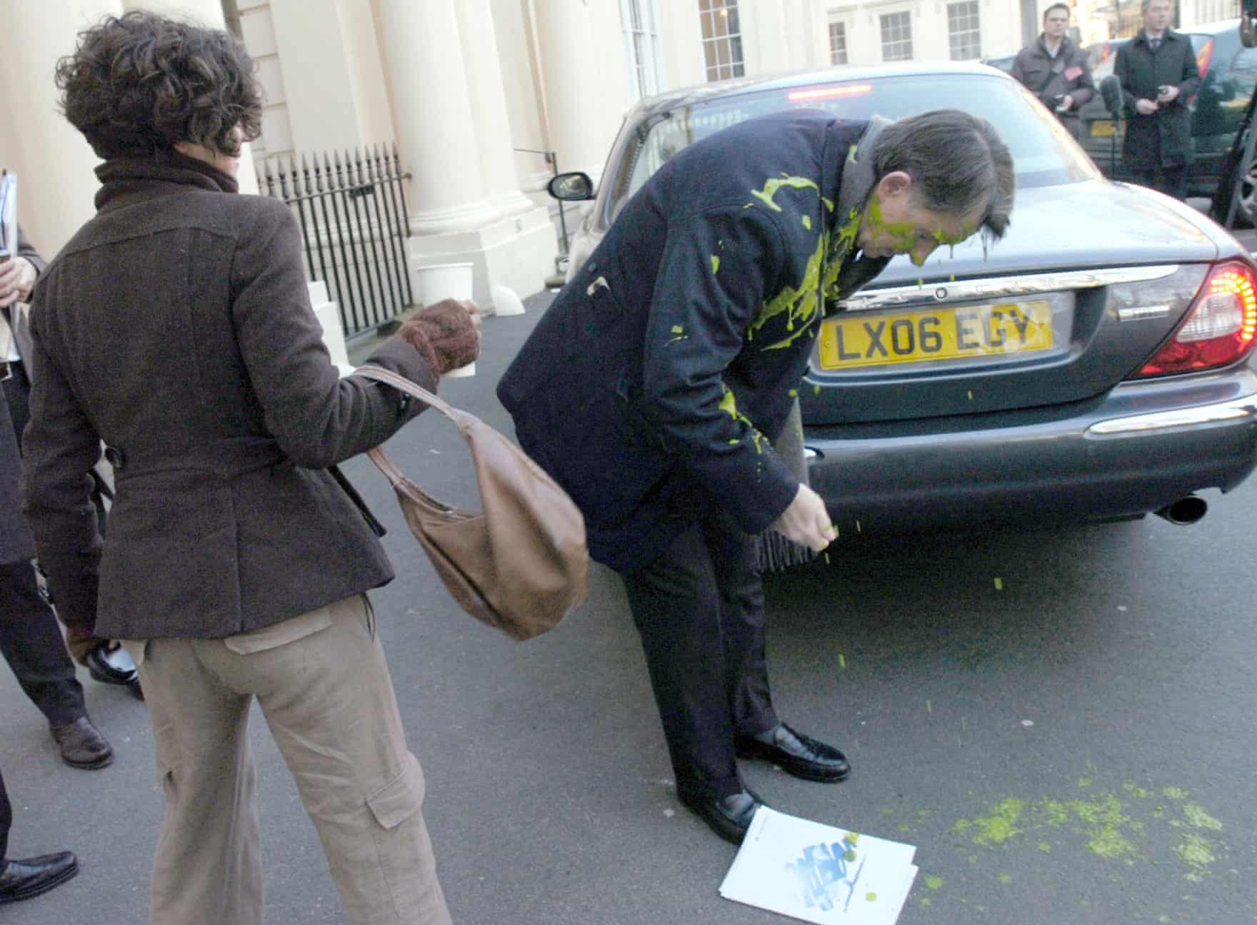 Peter Mandelson covered in custard by a protester, standing behind his Jaguar car.