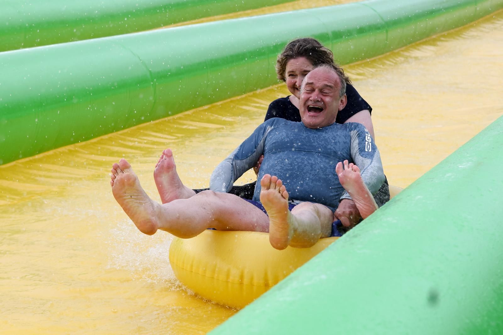 Ed Davey laughing while going down a water slide, enjoying a playful moment.