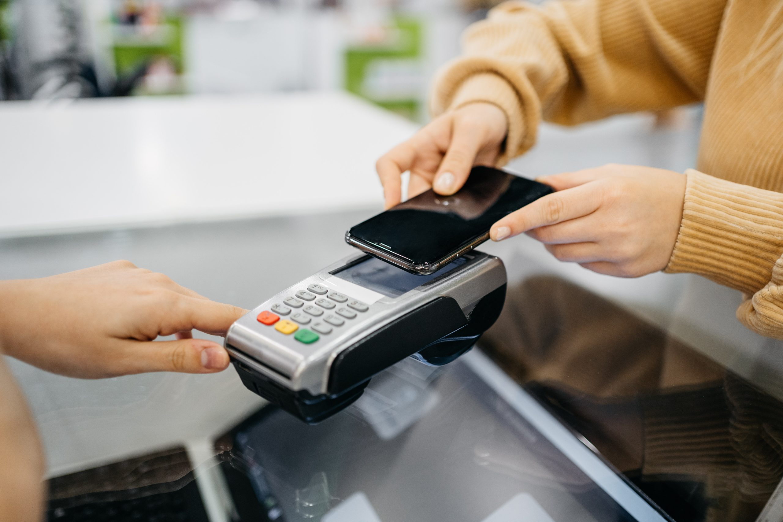 Person tapping their smartphone on a card reader to make a contactless payment.