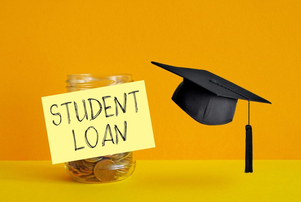 A graduation cap placed next to a jar labeled “Student Loan Savings,” symbolizing planning and saving for student loan repayment.