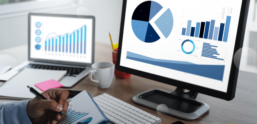 A business owner using pen, paper, and computer charts to gather financial data for a detailed business loan proposal.