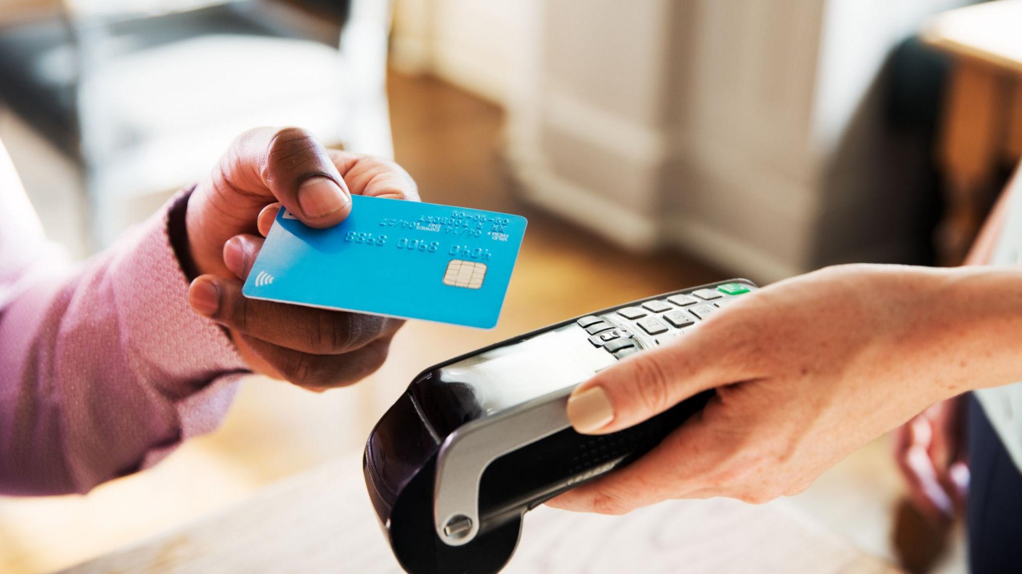 Customer tapping a bank card on a payment terminal to complete a contactless purchase.