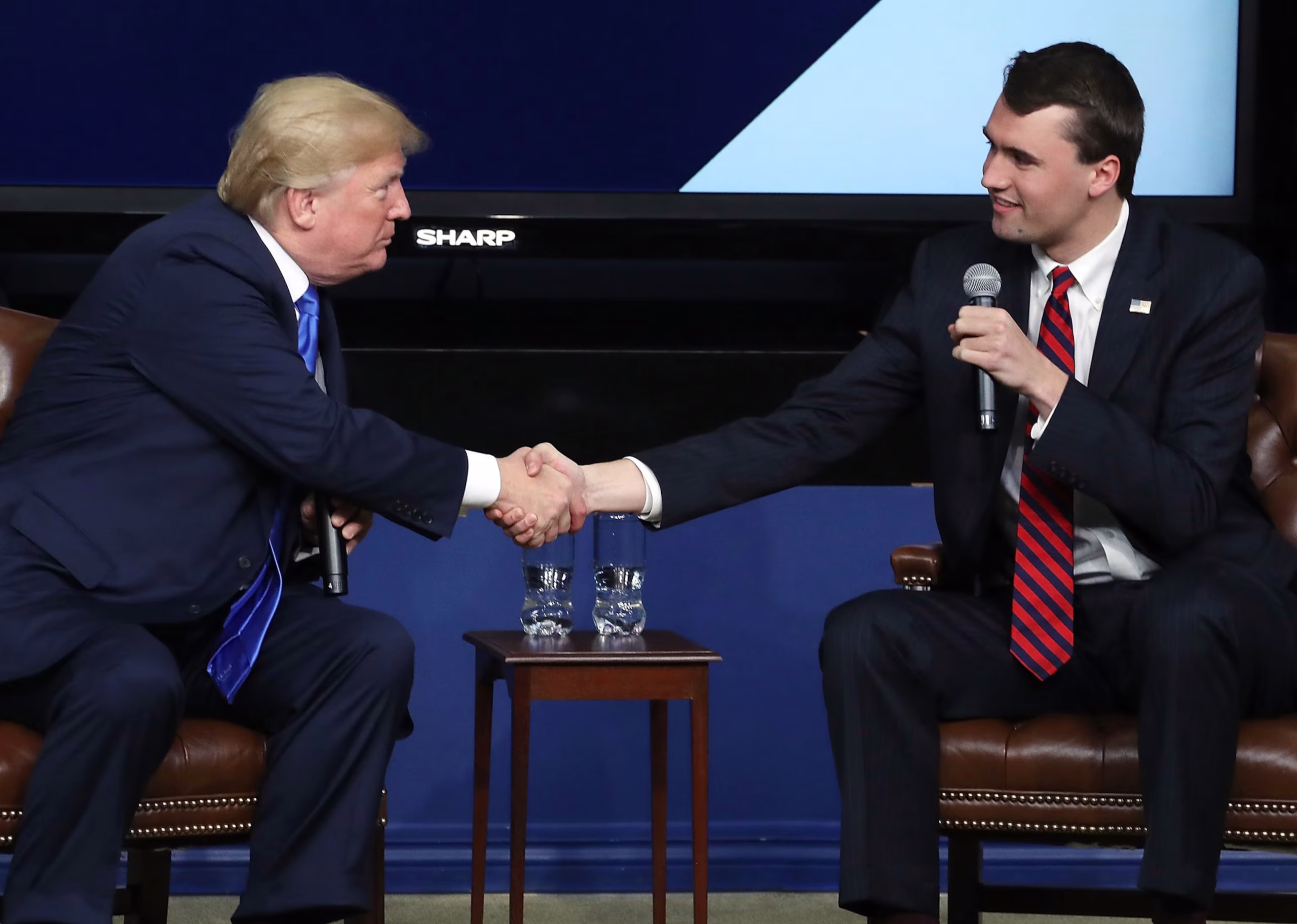 Charlie Kirk standing alongside President Donald Trump on stage at a pro-MAGA rally, addressing a cheering crowd.