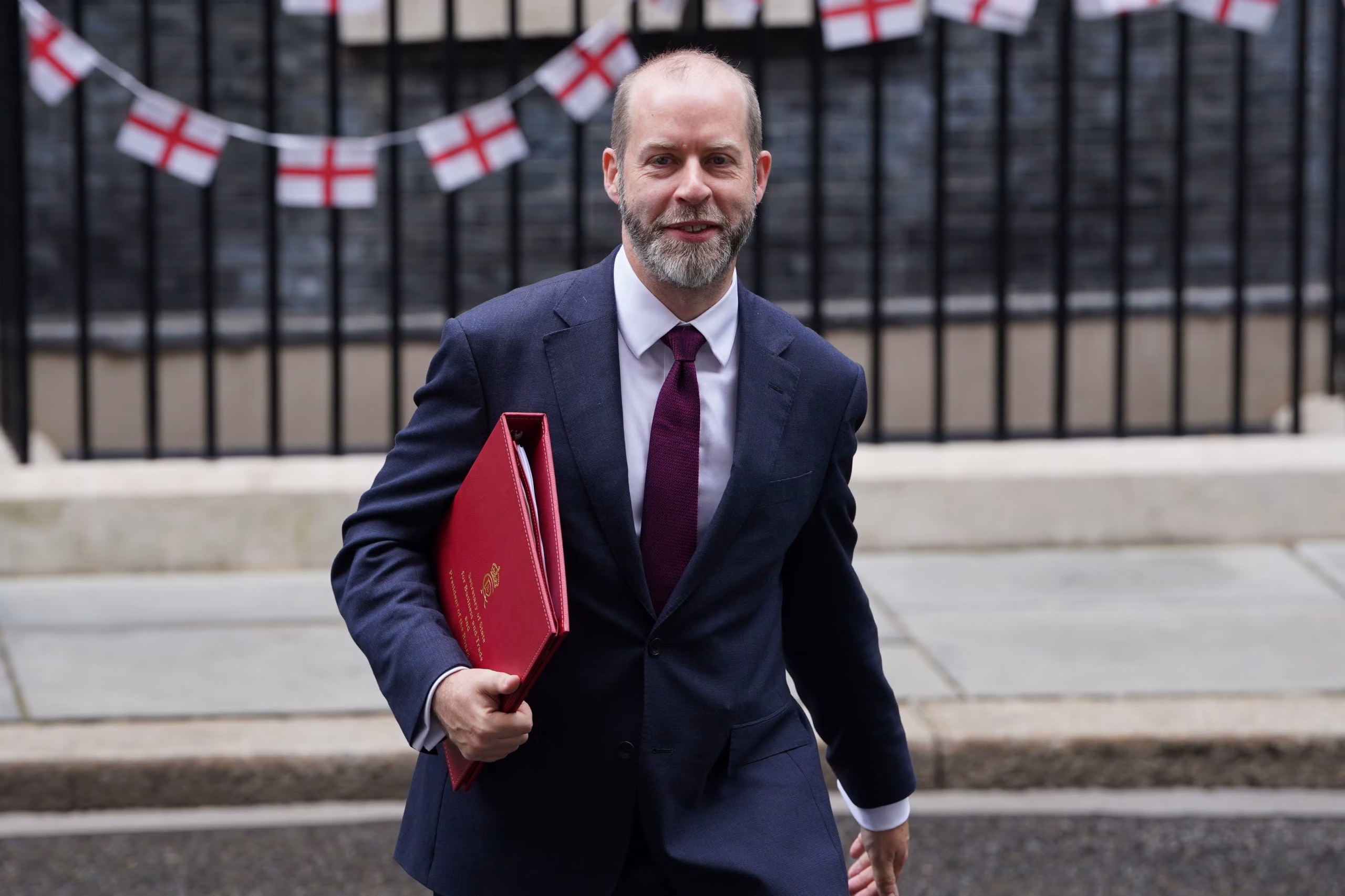 Jonathan Reynolds walking across Downing Street with a folder under his arm, England flags in the background.