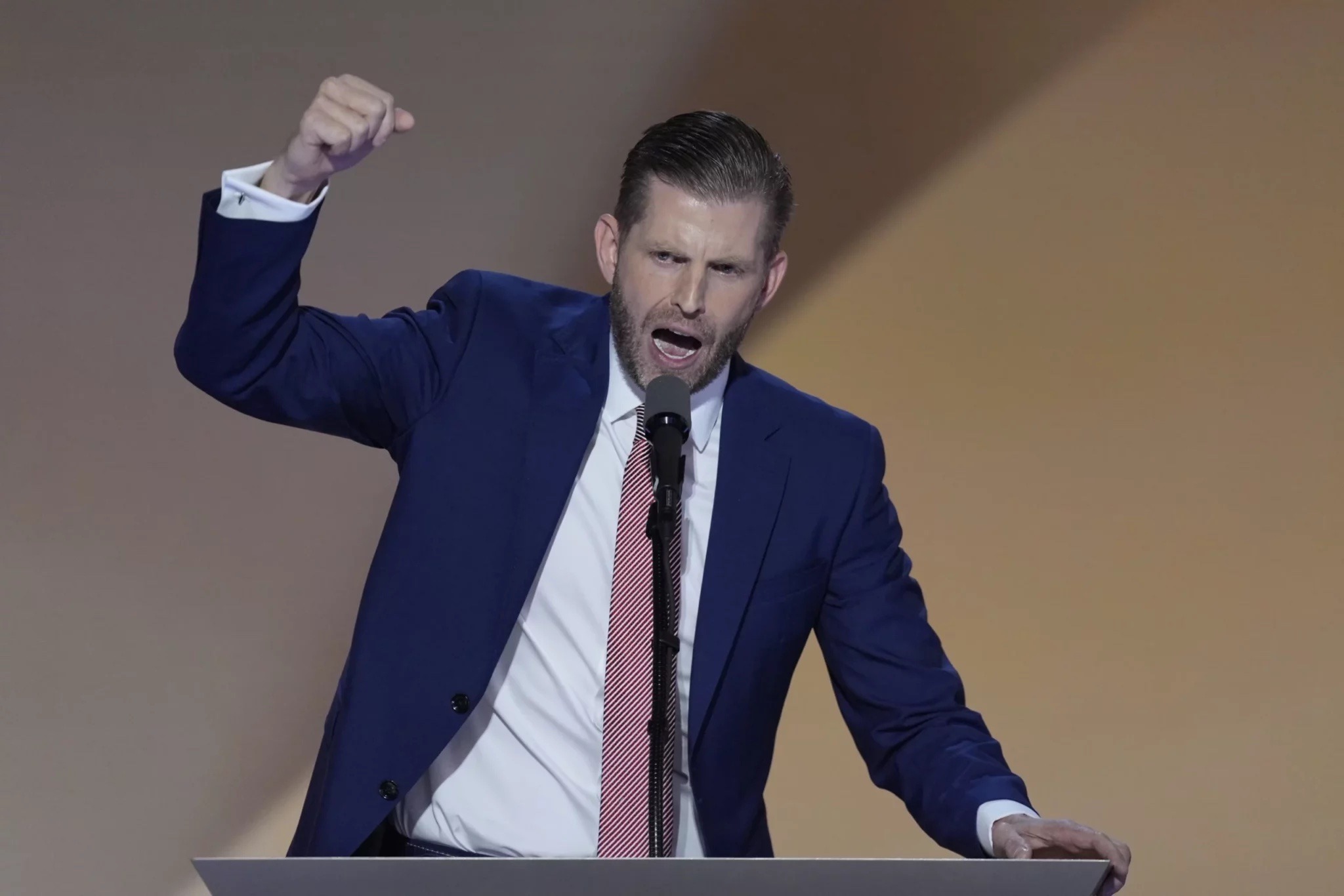 Eric Trump delivering a passionate speech at a podium, gesturing with intensity as he addresses the audience.