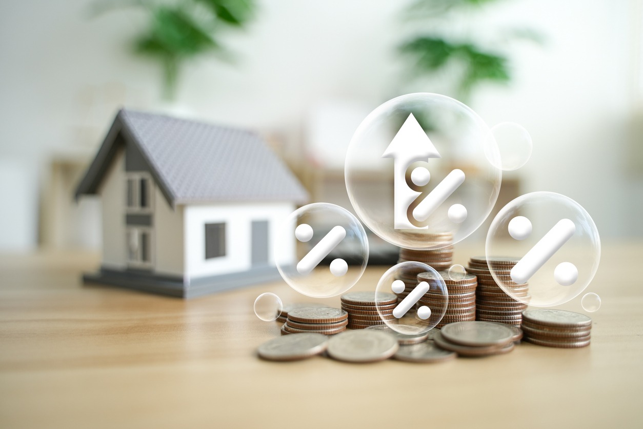 percentage symbol for interest rate increase on pile of coins and sample house. interest rate hikes, home loans, mortgages, home taxes. investment and asset management concepts.