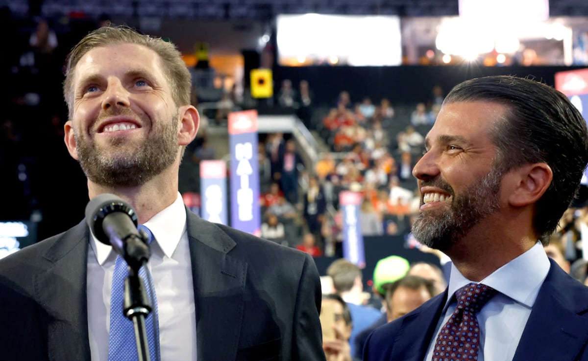 Eric Trump and Donald Trump Jr. smiling as they deliver a joint speech at a public event.